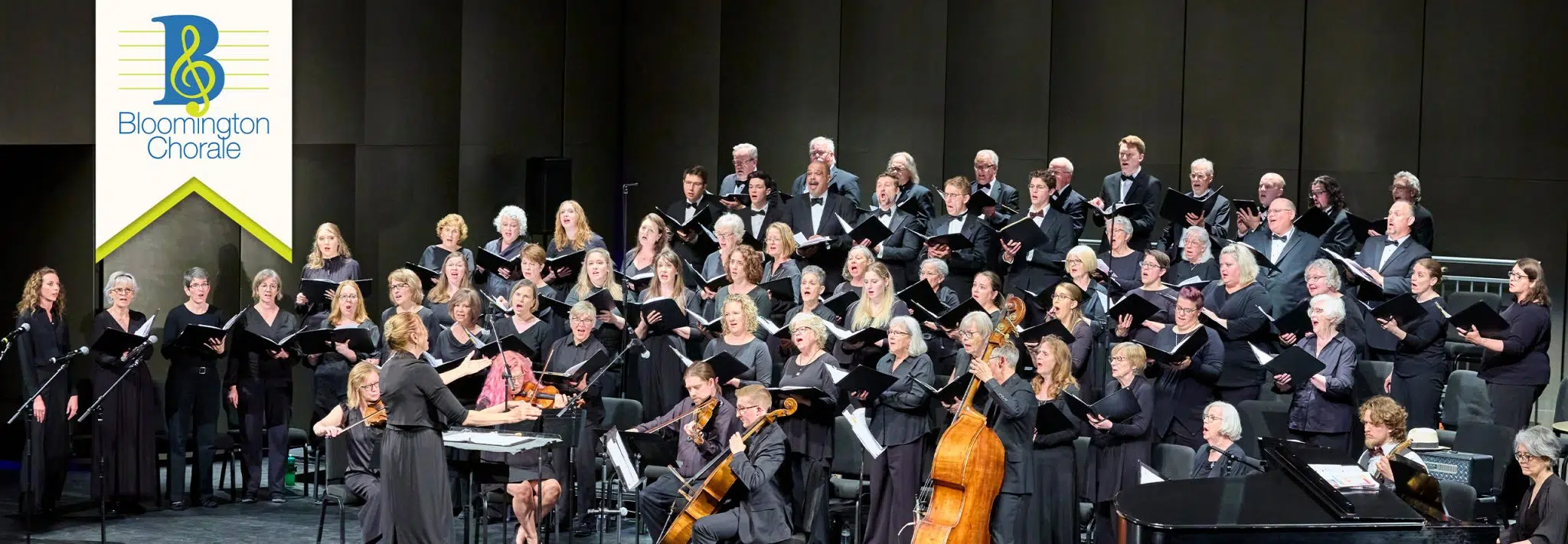 A choir wearing black robes sings on stage.