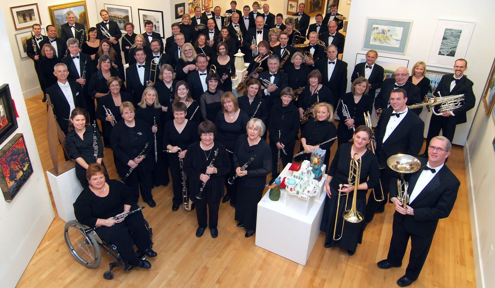 A group of people in tuxedos and fancy dresses hold their instruments and smile