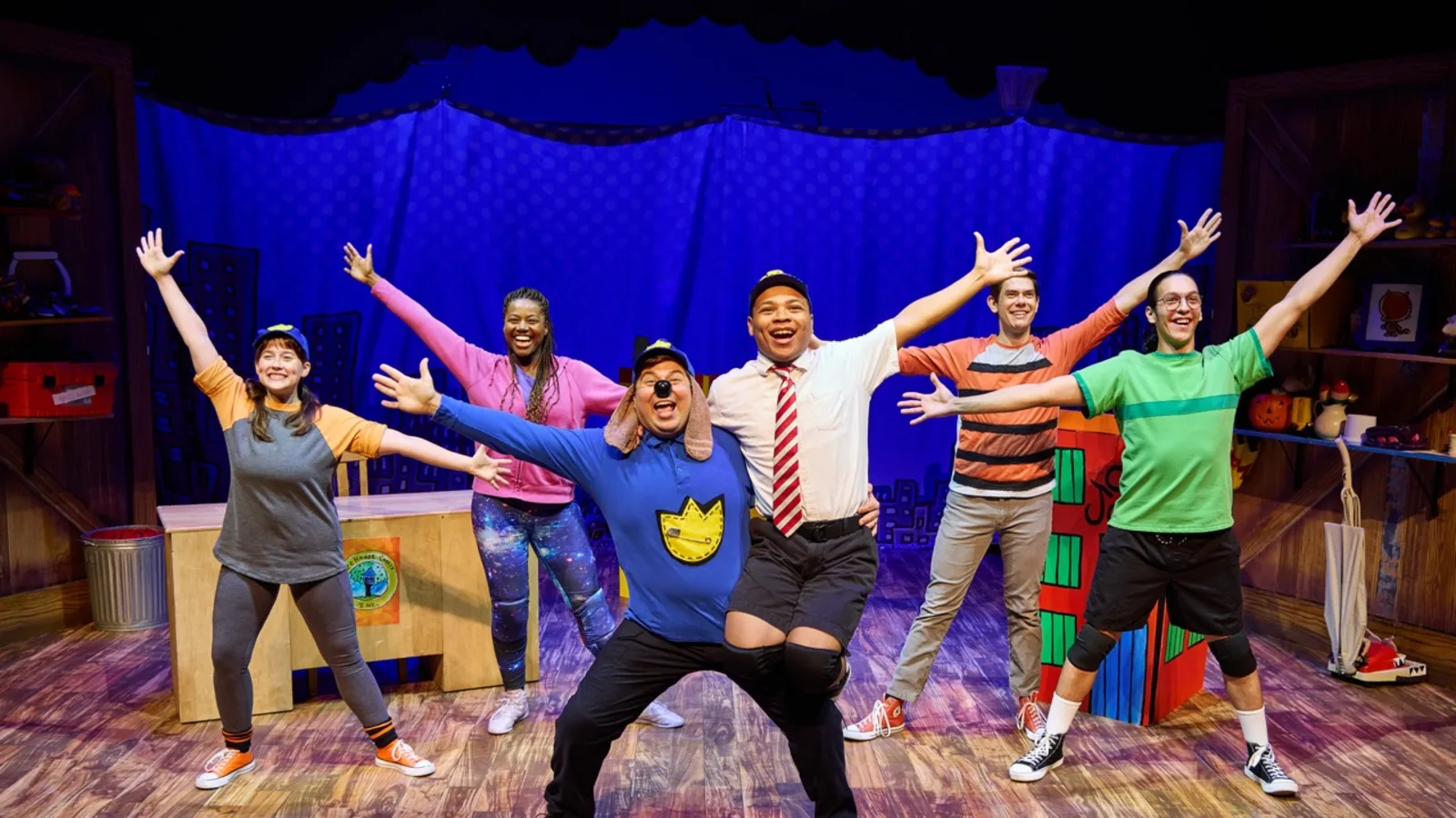 A group of stage performers in bright costumes strike a pose