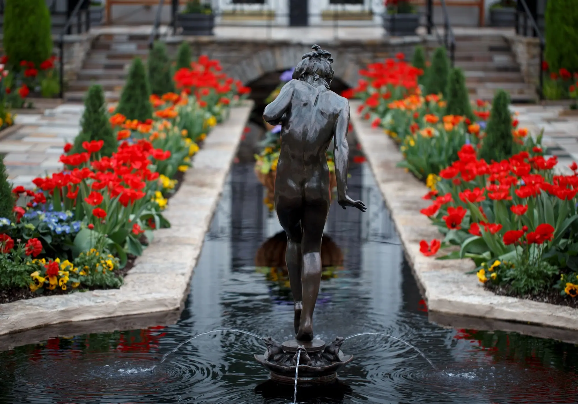 A statue in a fountain surrounded by bright spring flowers