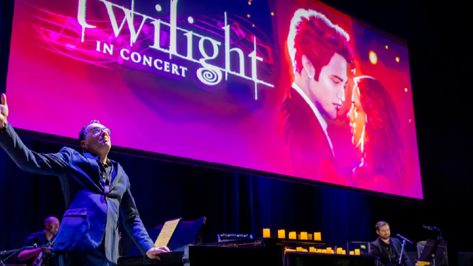 A conductor stands in front of a large screen that says Twilight in Concert