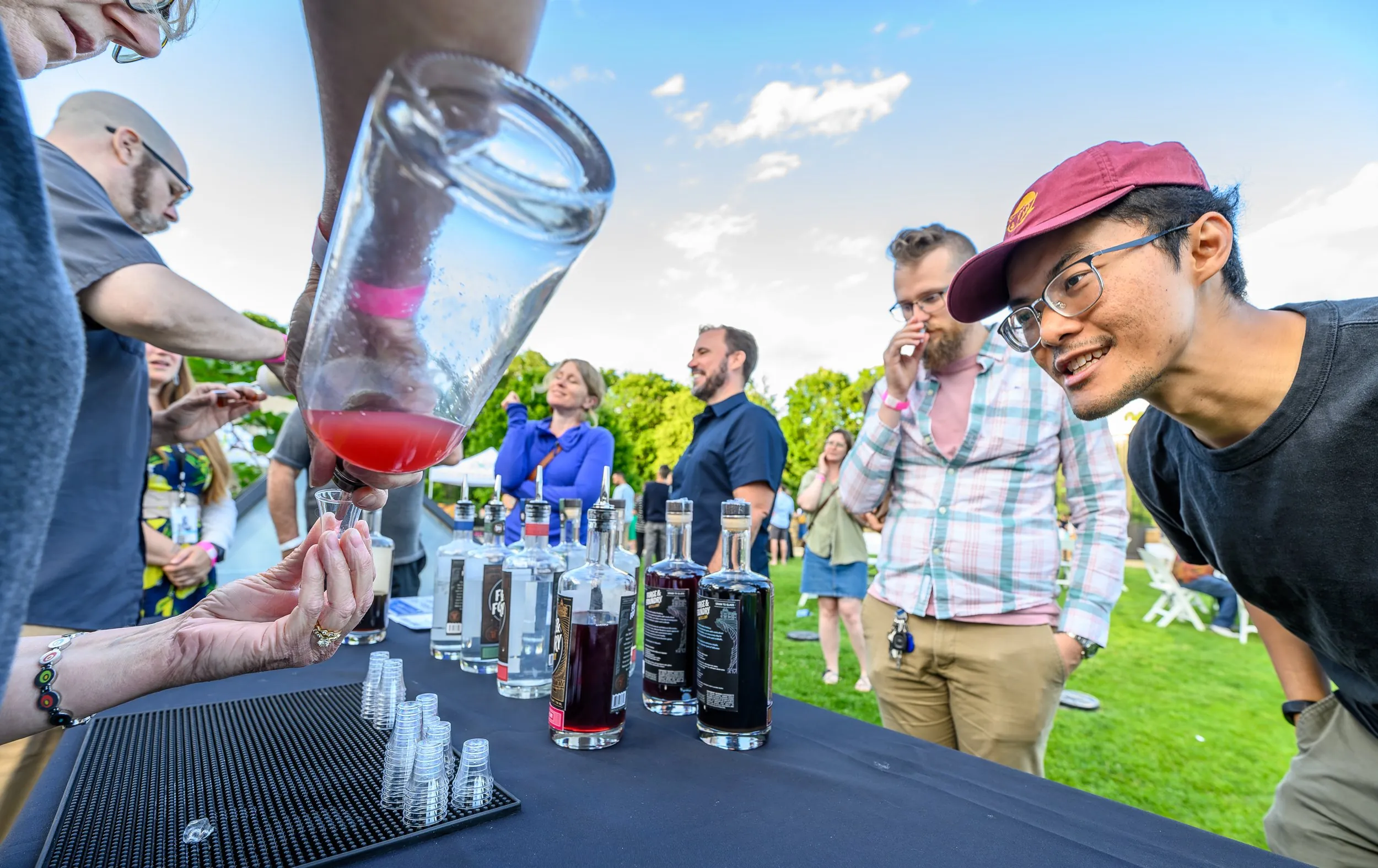 A man examines a bartender pouring a bright red shot of liquid