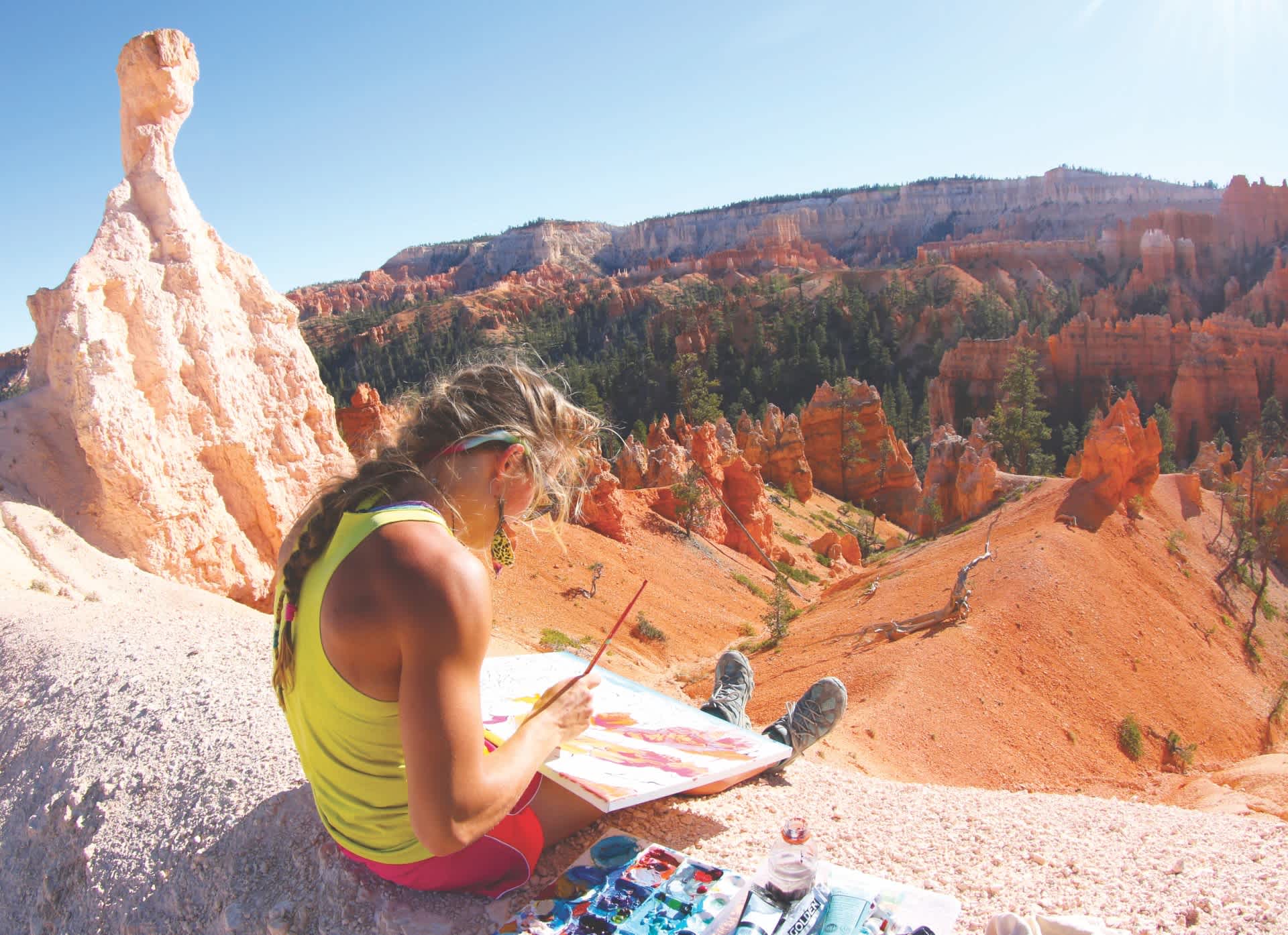A woman paints while sitting on top of a mountain