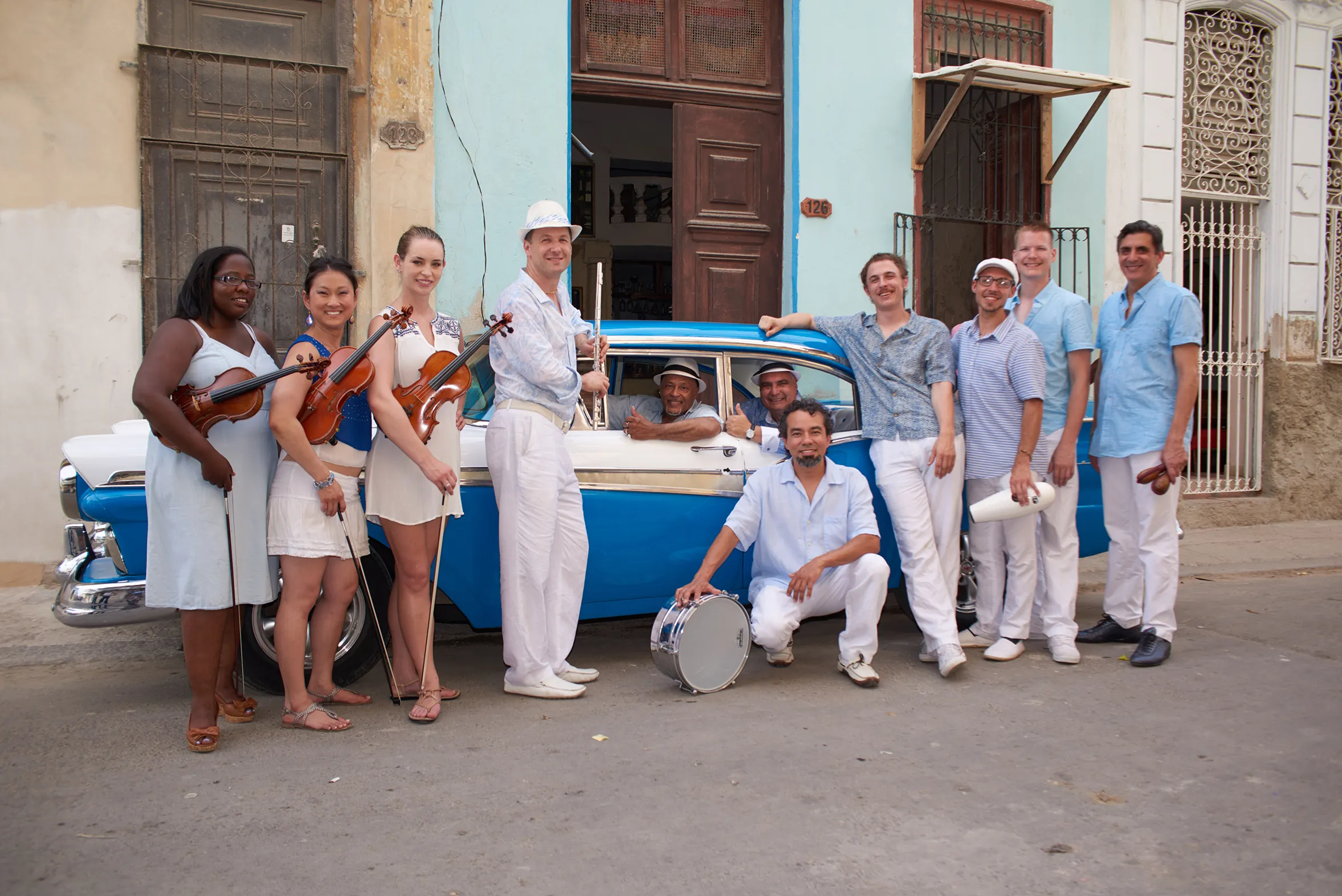 A group of musicians pose in front of a 1950s-era blue car