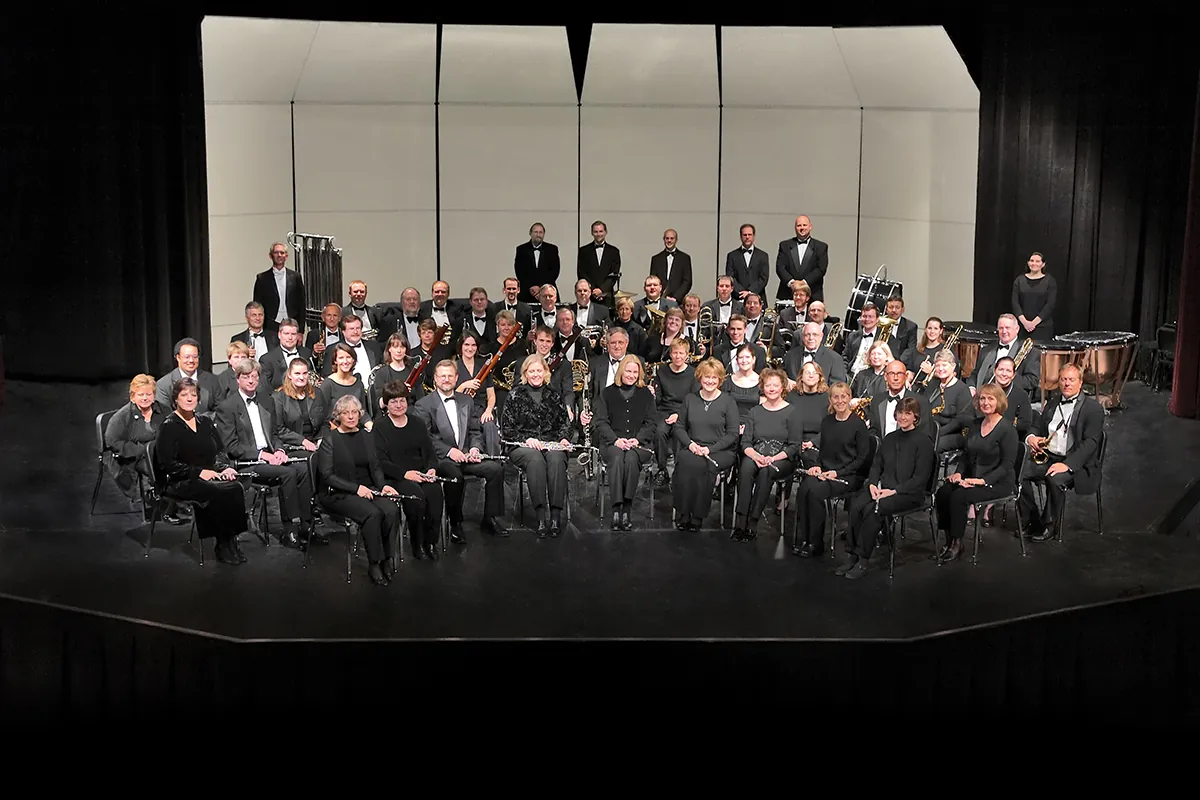 An orchestra dressed all in black sits with instruments in laps