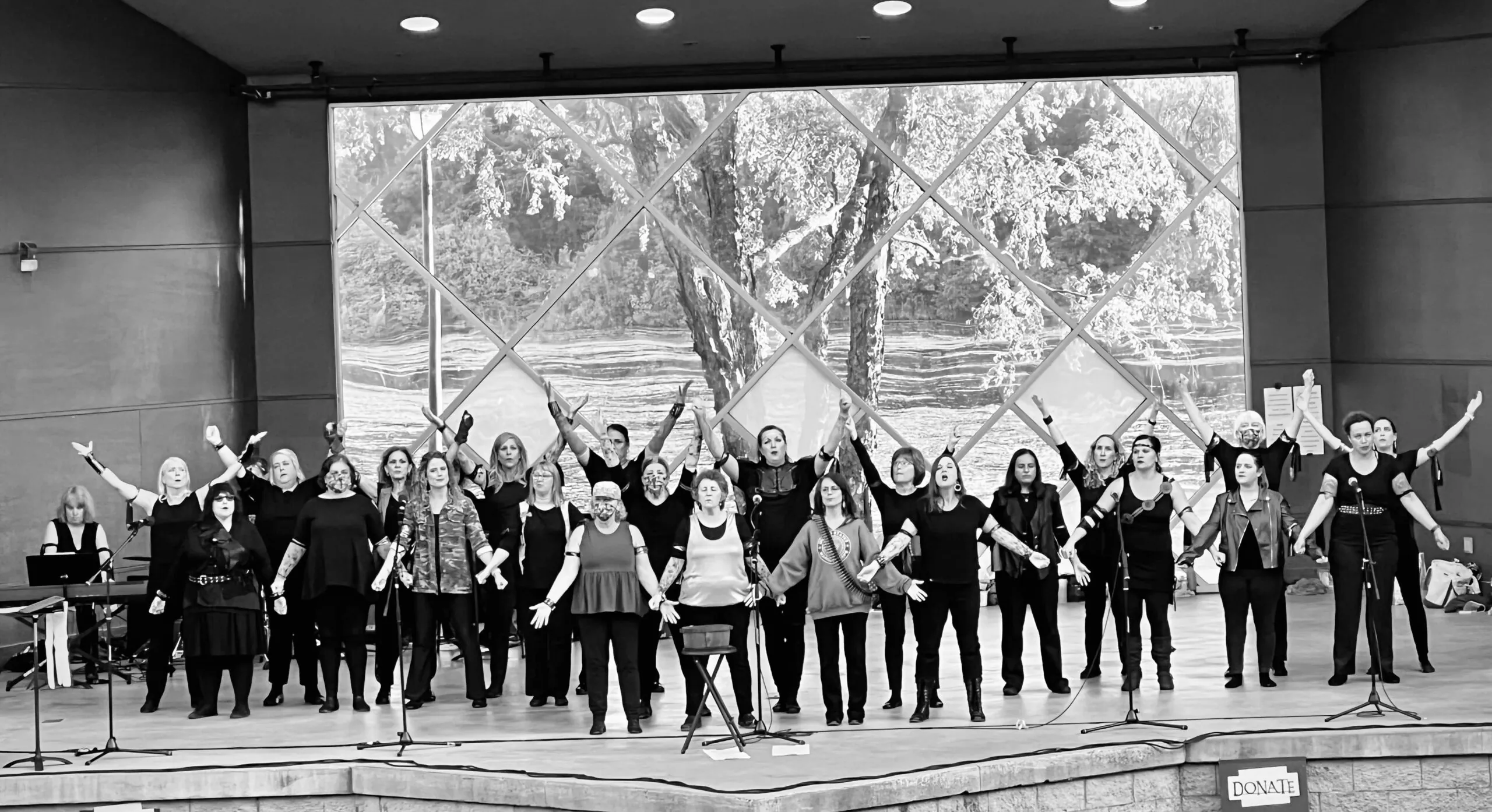 Black and white image of a female chorale group singing with their arms outstretched