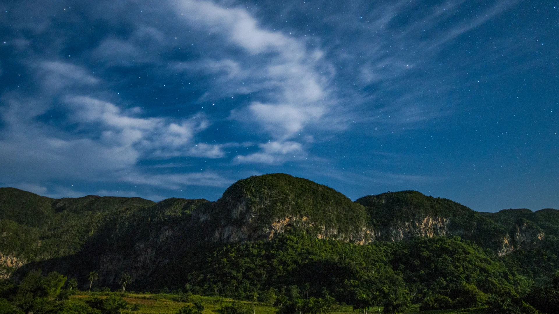 A green mountain range with twilight sky and stars in the background