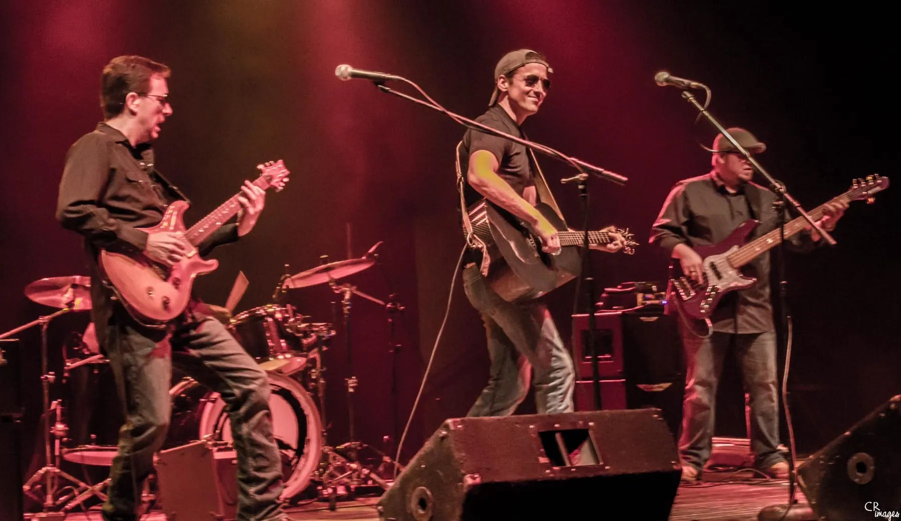 3 male musicians dressed in black play guitars on stage