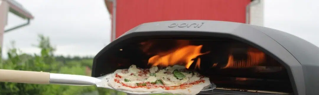 Pizza Nights at the Farm. An image of a pizza going into an outdoor pizza oven.